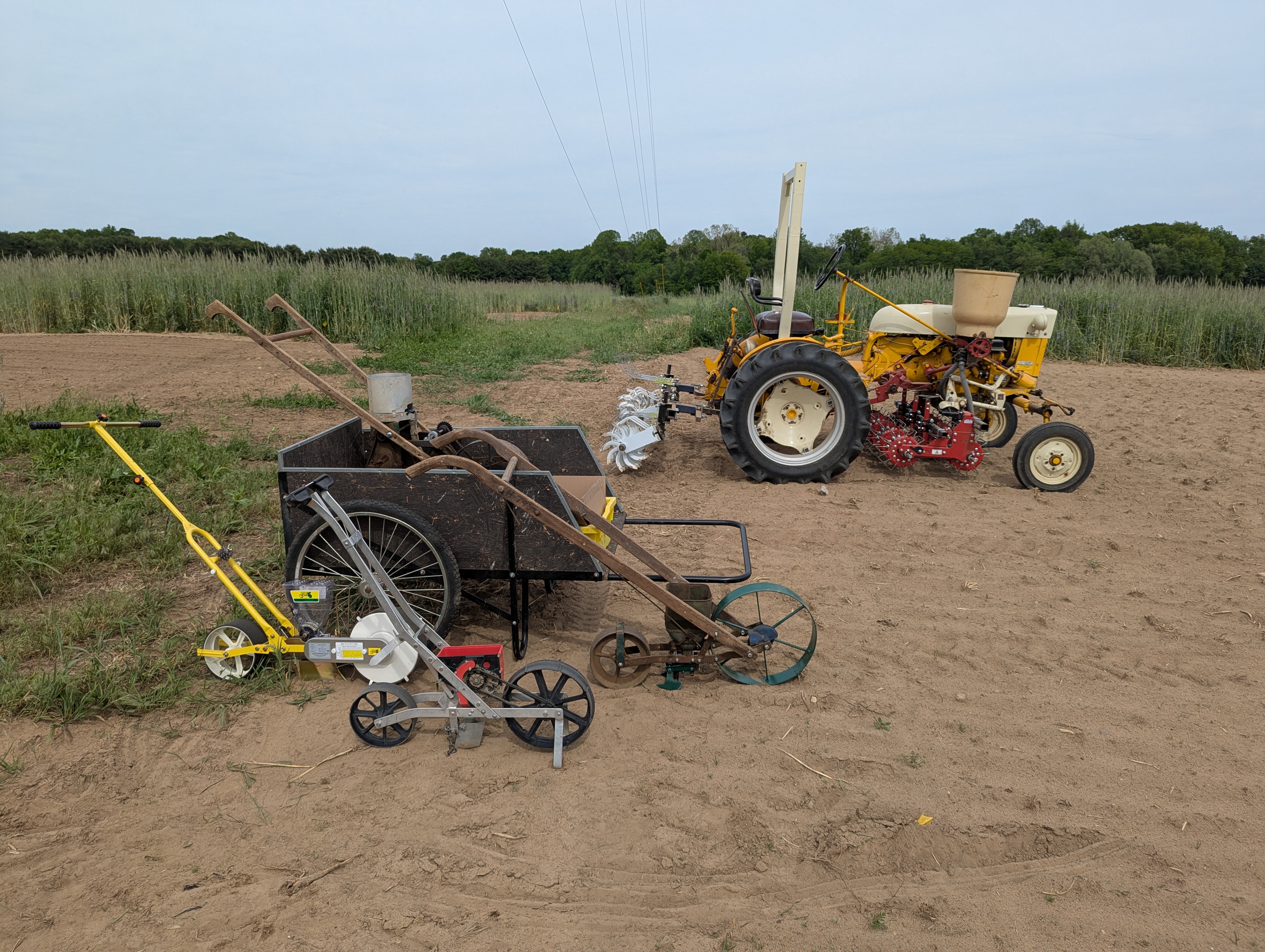 A small tractor with an implement and seeder carts with hand push handles.
